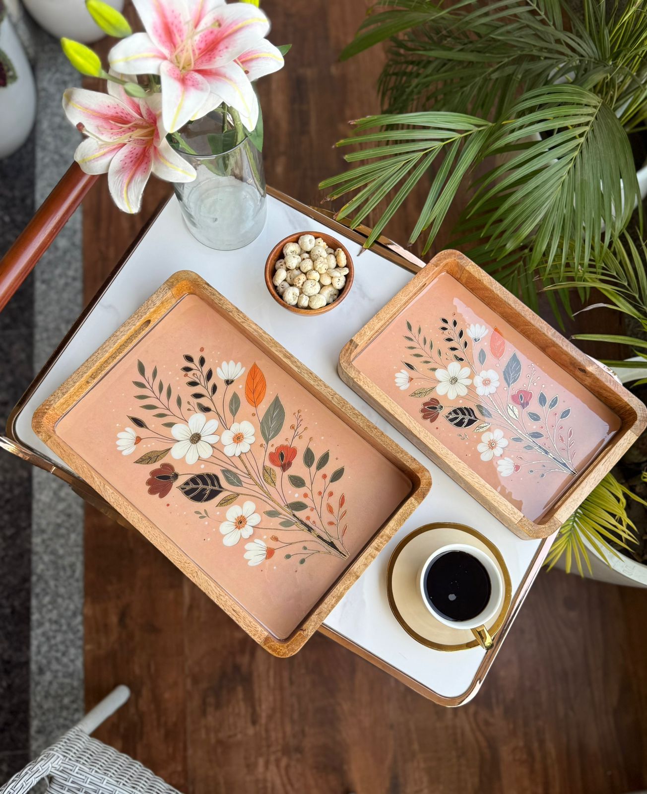 Decorative trays with floral designs on a table with a cup of coffee and flowers.